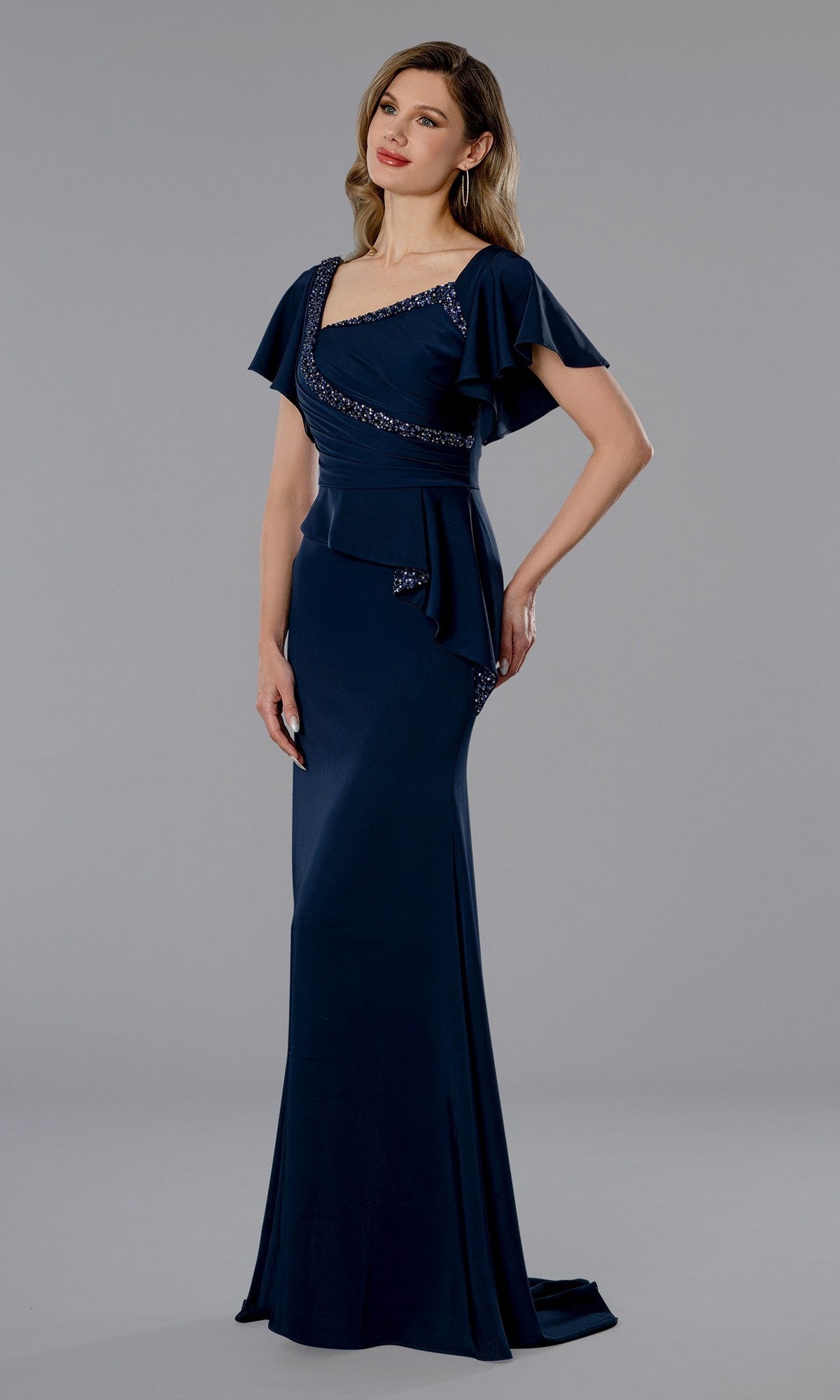 A woman models the Stella Couture 25352 long formal dress in navy, featuring flutter sleeves, a fitted waist, and an asymmetrical neckline with beaded accents.